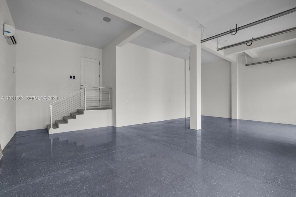Open-concept interior featuring high ceilings, epoxy-finished flooring, structural support columns, and an elevated staircase with horizontal cable railing
