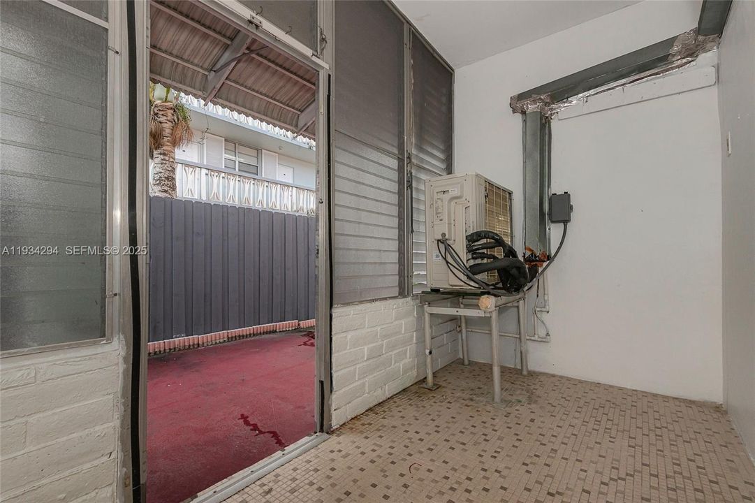 The Mini-split air conditioning unit shares a part of the enclosed porch as it cools the entire condominium unit. with the door open, you can see part of the red patio behind this unit.