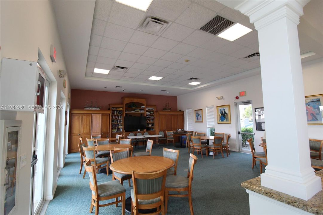 Open-concept common area featuring a dropped tile ceiling with recessed lighting, integrated wood cabinetry, a decorative column, and natural stone-surface countertops