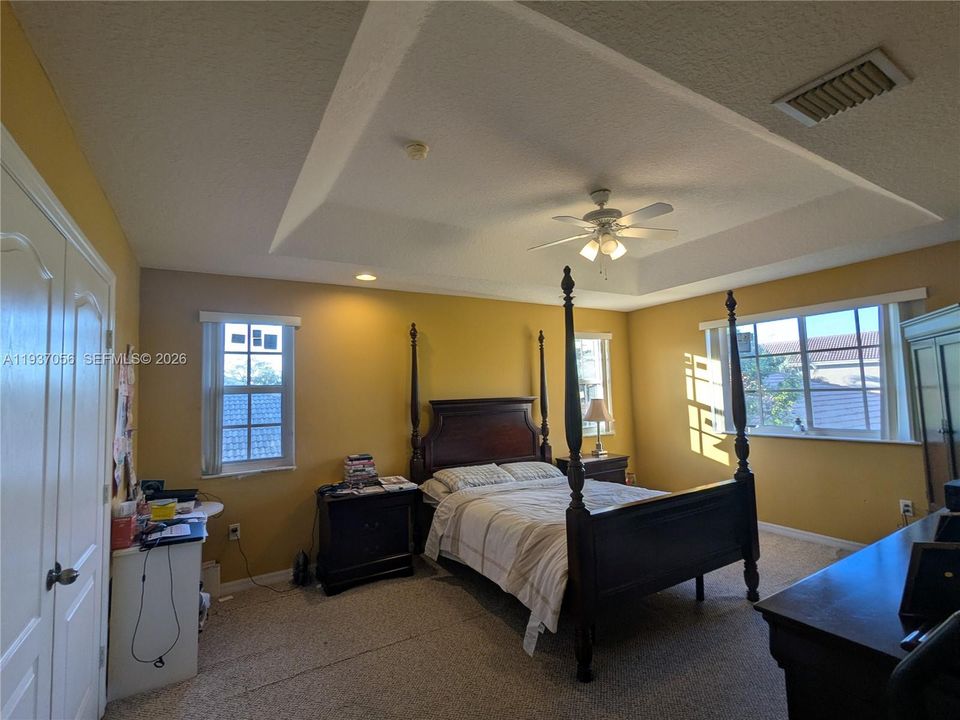 Spacious primary bedroom featuring a dramatic tray ceiling and plenty of natural light