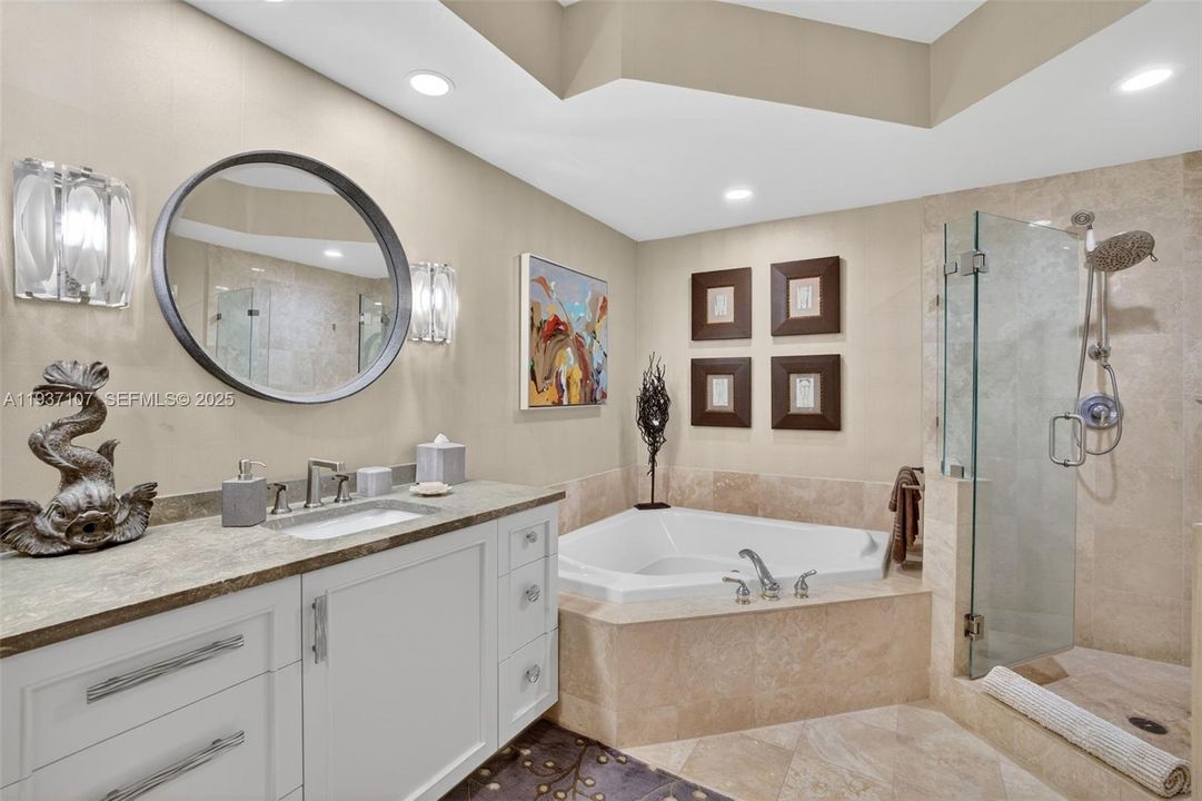 Primary bathroom w/ custom wood vanity & upgraded hardware. Beautiful stone vanity counter, wall coverings, sconces, separate jetted tub & shower