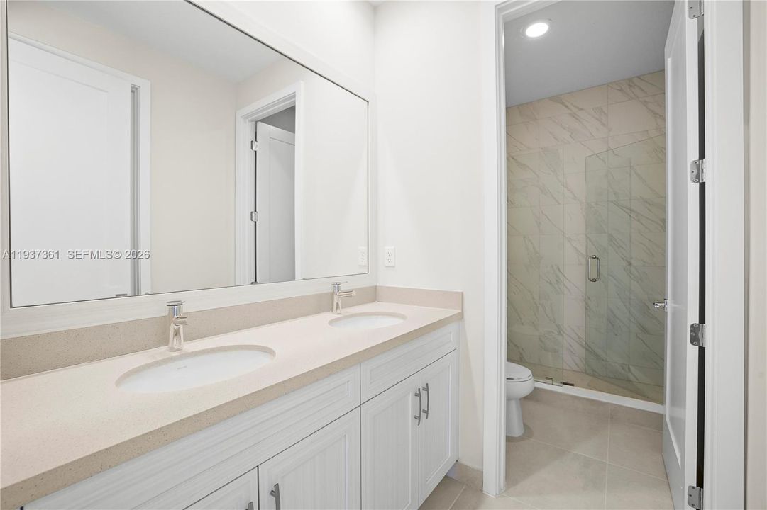 Jack-and-Jill bathroom with dual vanities, glass-enclosed shower, and tile flooring