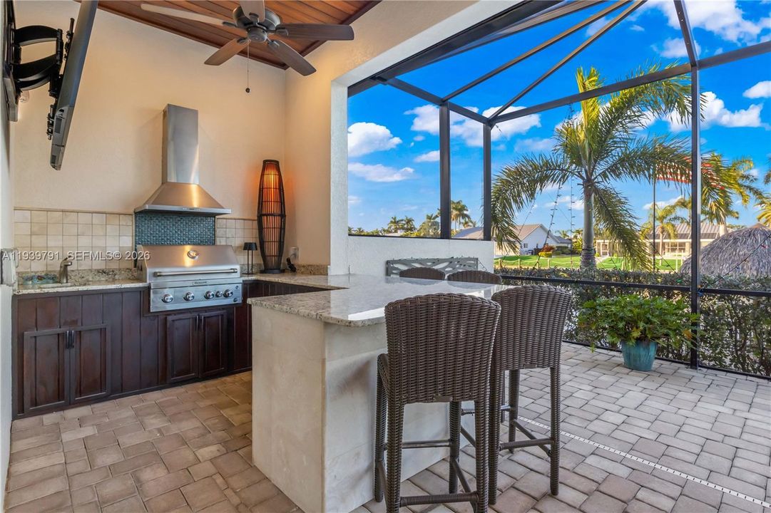 Fully equipped outdoor kitchen with grill, granite countertops, and bar seating, ideal for hosting gatherings.