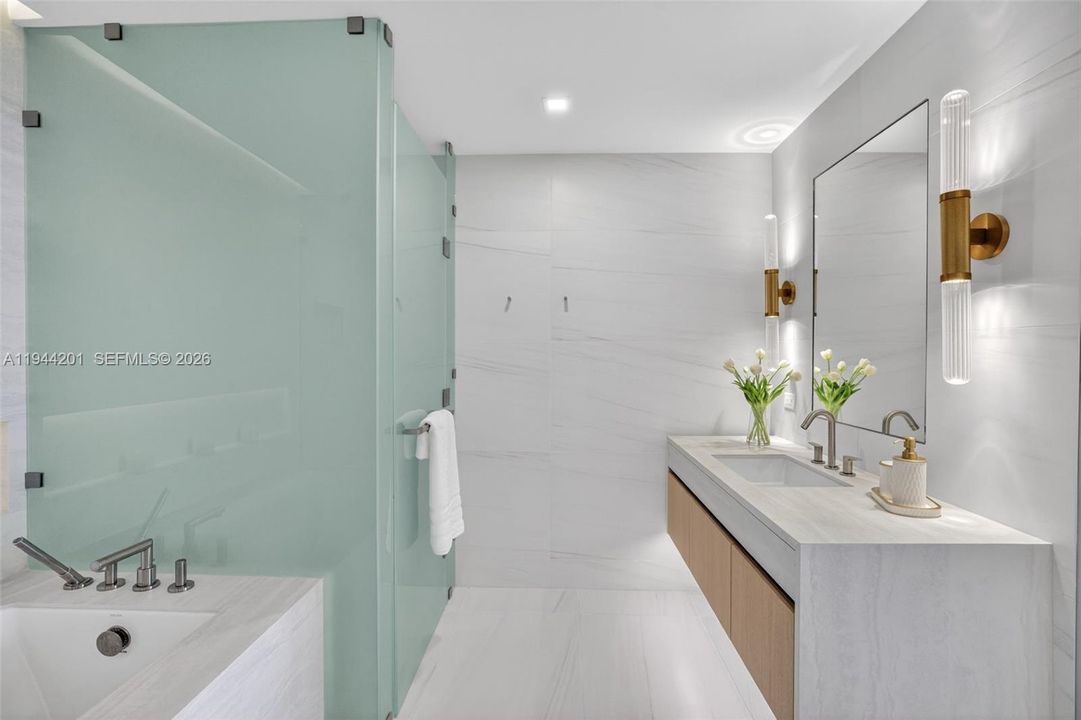 The 06 line primary bath feels like a private spa. Oversized and beautifully proportioned, it features a frameless glass walk in shower, designer soaking tub, dual vanities with stone counters, and sleek modern fixtures. Clean architectural lines, neutral luxury finishes, and generous storage for a calm, resort style retreat that complements the open coastal aesthetic of the residence.