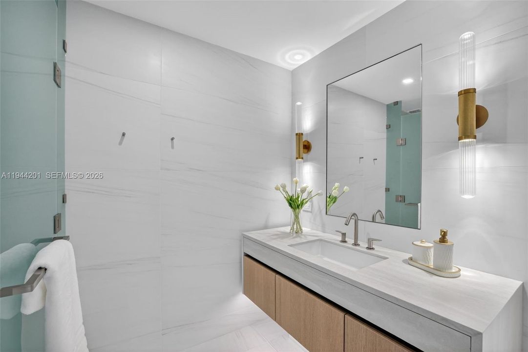 The 06 line primary bath feels like a private spa. Oversized and beautifully proportioned, it features a frameless glass walk in shower, designer soaking tub, dual vanities with stone counters, and sleek modern fixtures. Clean architectural lines, neutral luxury finishes, and generous storage for a calm, resort style retreat that complements the open coastal aesthetic of the residence.