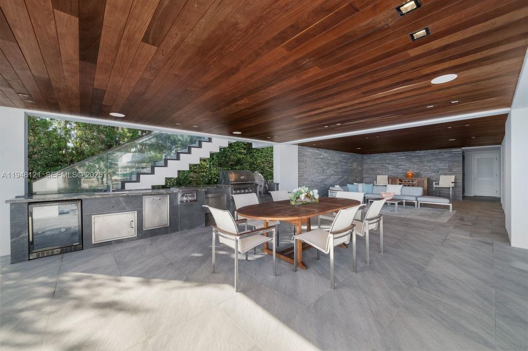 Outdoor kitchen fully appointed with grill, sink, refrigerator, and several lounge areas for shaded outdoor entertaining.