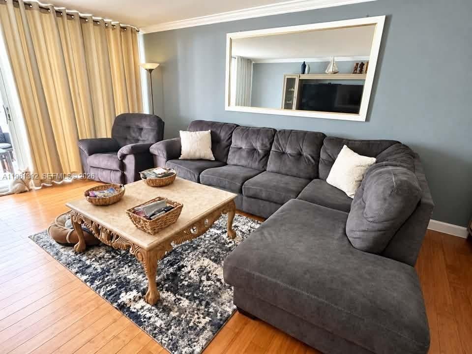 Living area featuring wood-finish flooring, crown molding, and large wall-mounted mirror