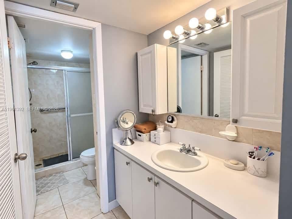 Bathroom featuring a white vanity cabinet with an integrated sink, wall-mounted medicine cabinets, a multi-bulb vanity light fixture, and a walk-in shower with a glass door and tiled surround