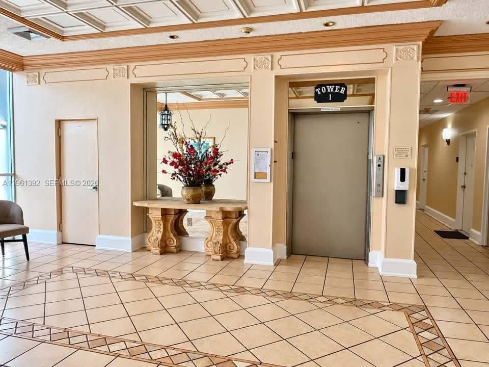 Lobby area featuring tile flooring with decorative inlay, coffered ceiling, inset wall mirror, and elevator access