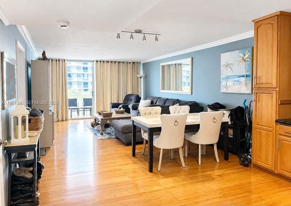Open living area featuring wood-finish flooring, crown molding, track lighting, and tall wood cabinetry