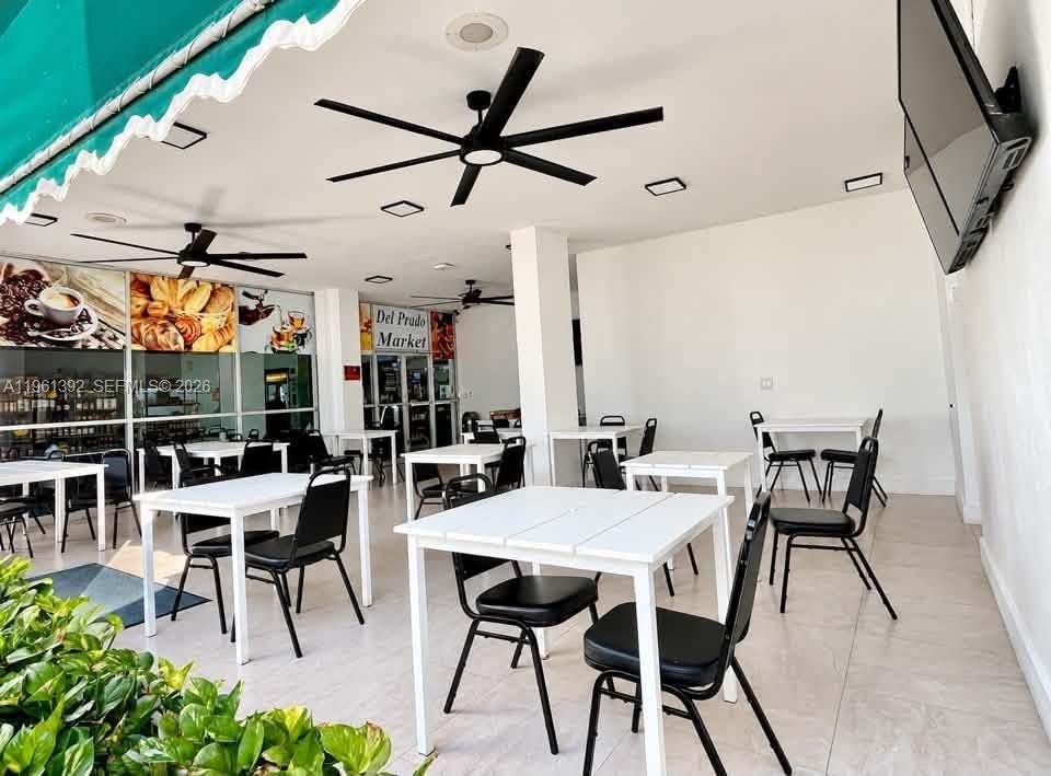 Covered outdoor area featuring neutral tile flooring, recessed lighting, multiple matte black ceiling fans, and a retractable green awning