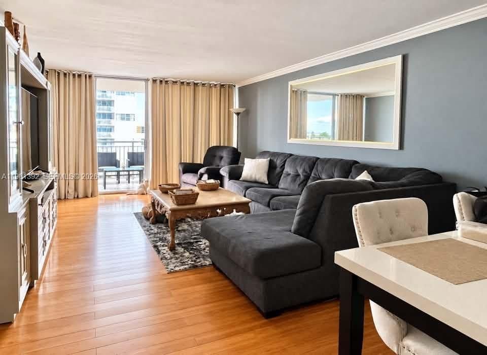 Living area featuring wood-finish flooring, crown molding, and a sliding glass door providing access to a balcony
