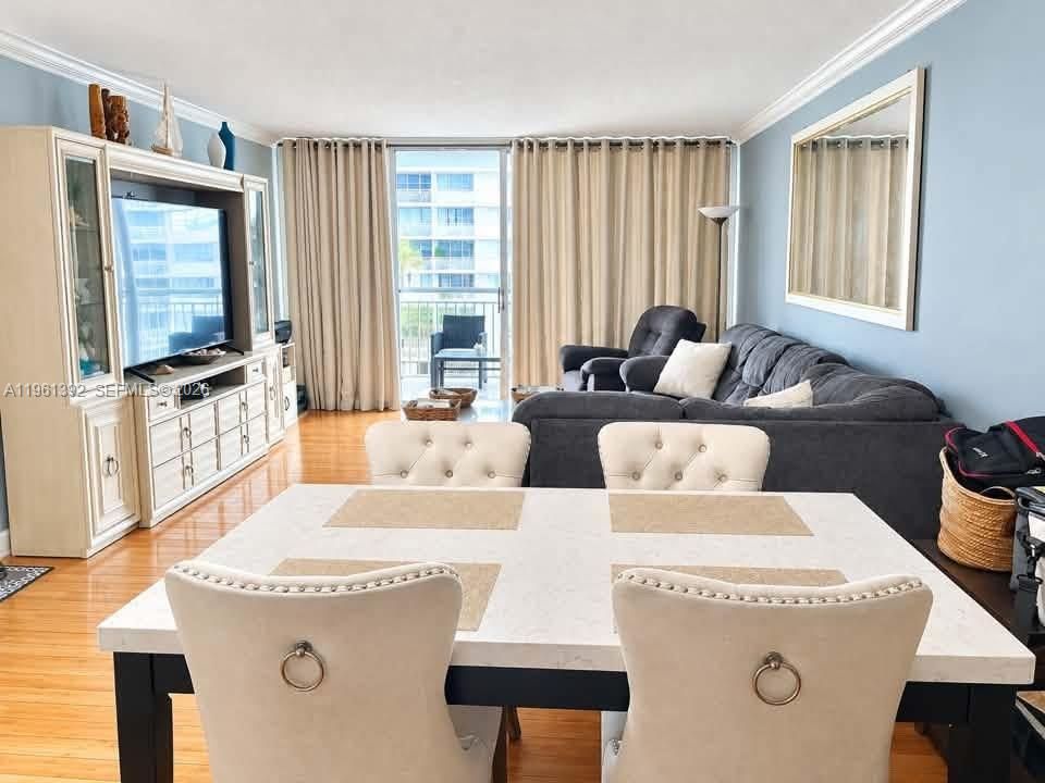 Open-concept living space featuring wood-finish flooring, crown molding, built-in cabinetry, and sliding glass doors with balcony access