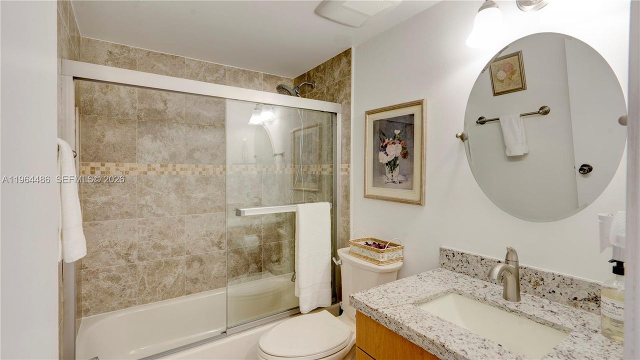 Guest bathroom totally remodeled with beautiful tiles and modern fixtures, bathtub with shower enclosure, custom cabinet and modern mirror