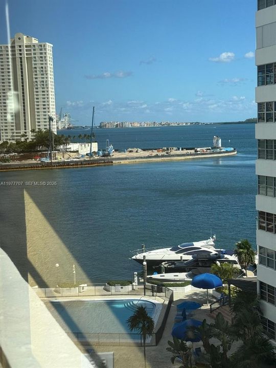 Waterfront balcony featuring a pool, surrounding hardscaped patio, and direct exposure to the bay and harbor