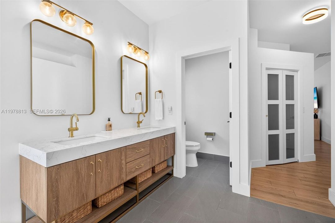 Primary suite with spa-like bathroom featuring double vanity, tile plank floors, private toilet