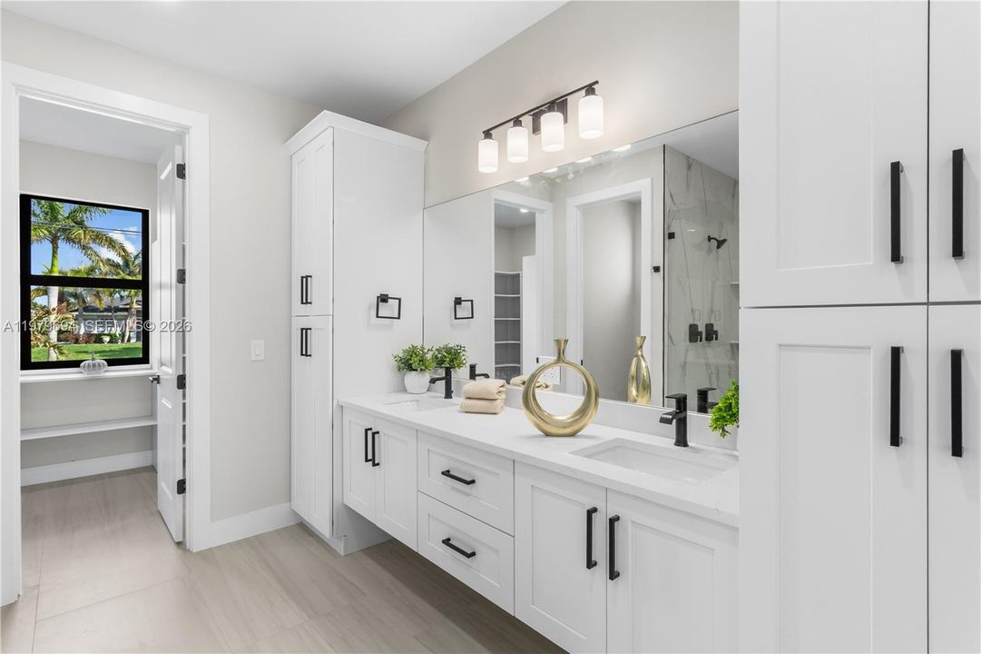 Dual-sink vanity w/ quartz countertops, sleek white cabinetry & contemporary lighting complements the spa-like design.