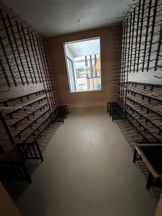 Custom climate-controlled wine room featuring floor-to-ceiling metal racking systems, wood-paneled walls,  and a large window looking onto the dining room