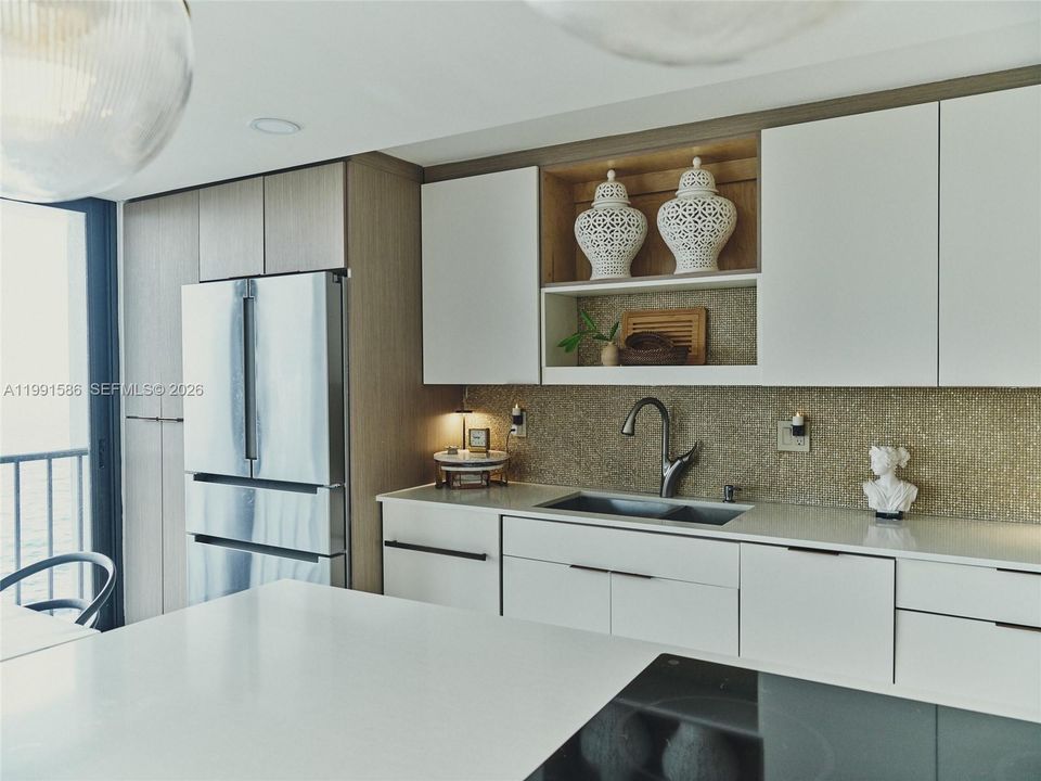 Custom designed kitchen with spacious snack seating peninsula.  Counter depth BOSCH refrigerator, drawer microwave, downdraft extractor, induction cooktop, floor to ceiling pantry with pull outs, touch-less faucet, metal backsplash, custom cabinetry.
