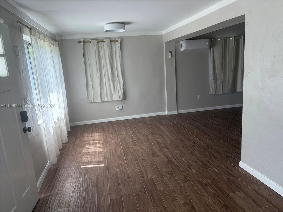 Interior space featuring wood-finish flooring, a wall-mounted ductless mini-split HVAC unit, neutral-toned walls, and a minimalist flush-mount ceiling light fixture