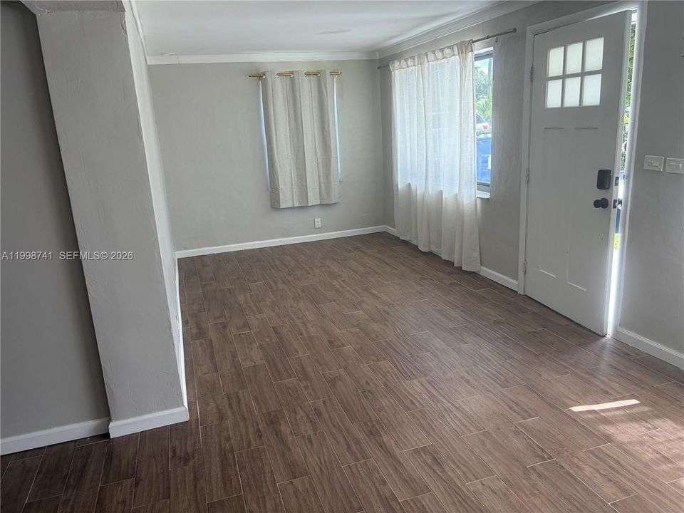 Living area featuring wood-finish flooring, neutral wall paint, crown molding, and an exterior door with a multi-pane glass insert