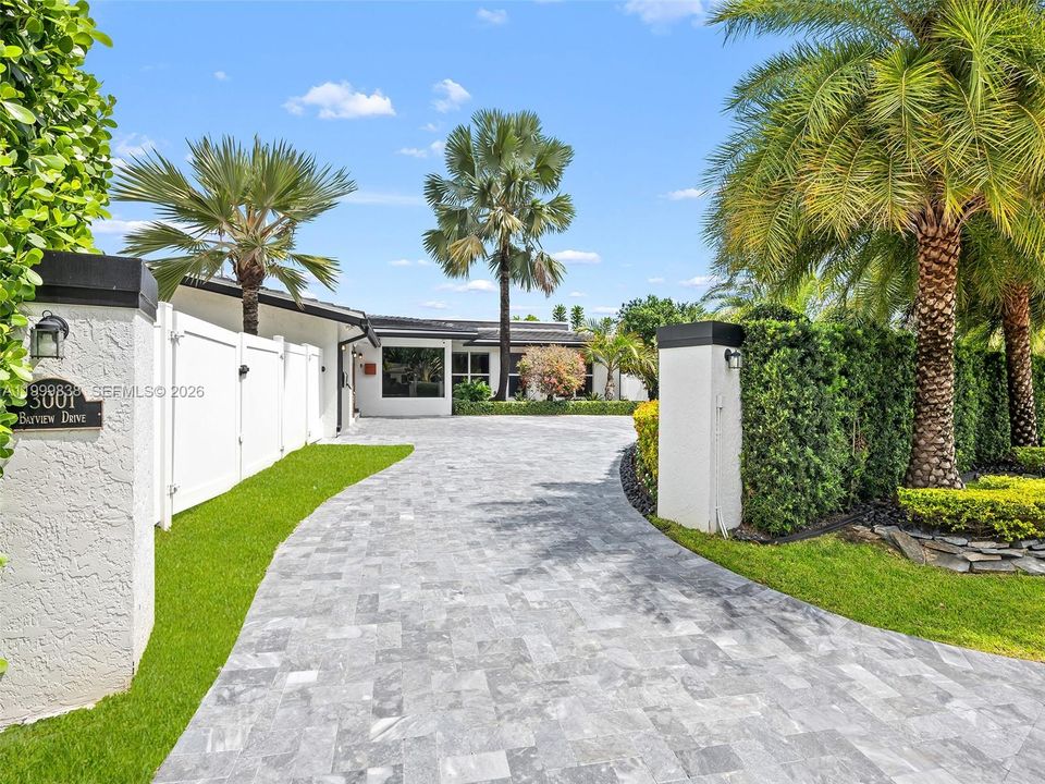 Walled entry with expansive driveway and lush landscaping