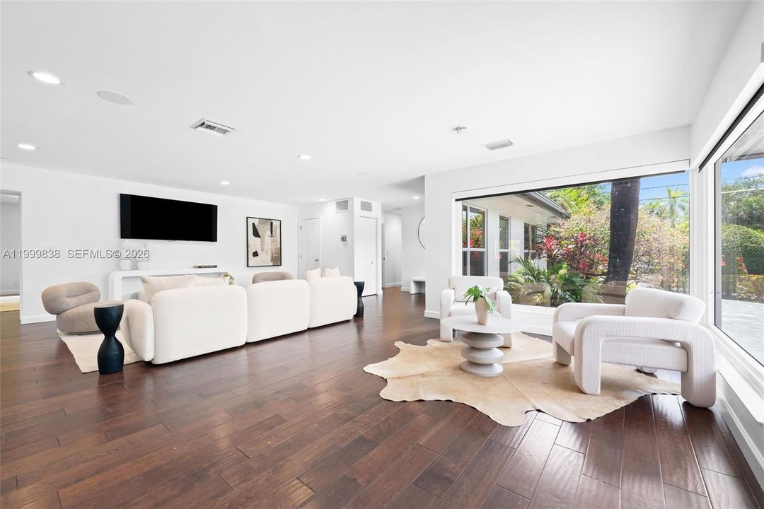 View of living area from front door featuring large floor to ceiling picture windows & hardwood flooring throughout.
