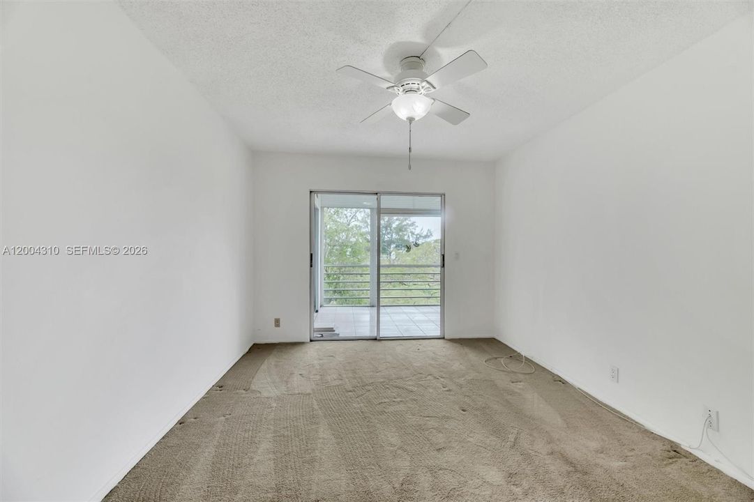 Bedroom with sliding glass door to porch, ceiling fan, tree/greenery views through glass.
