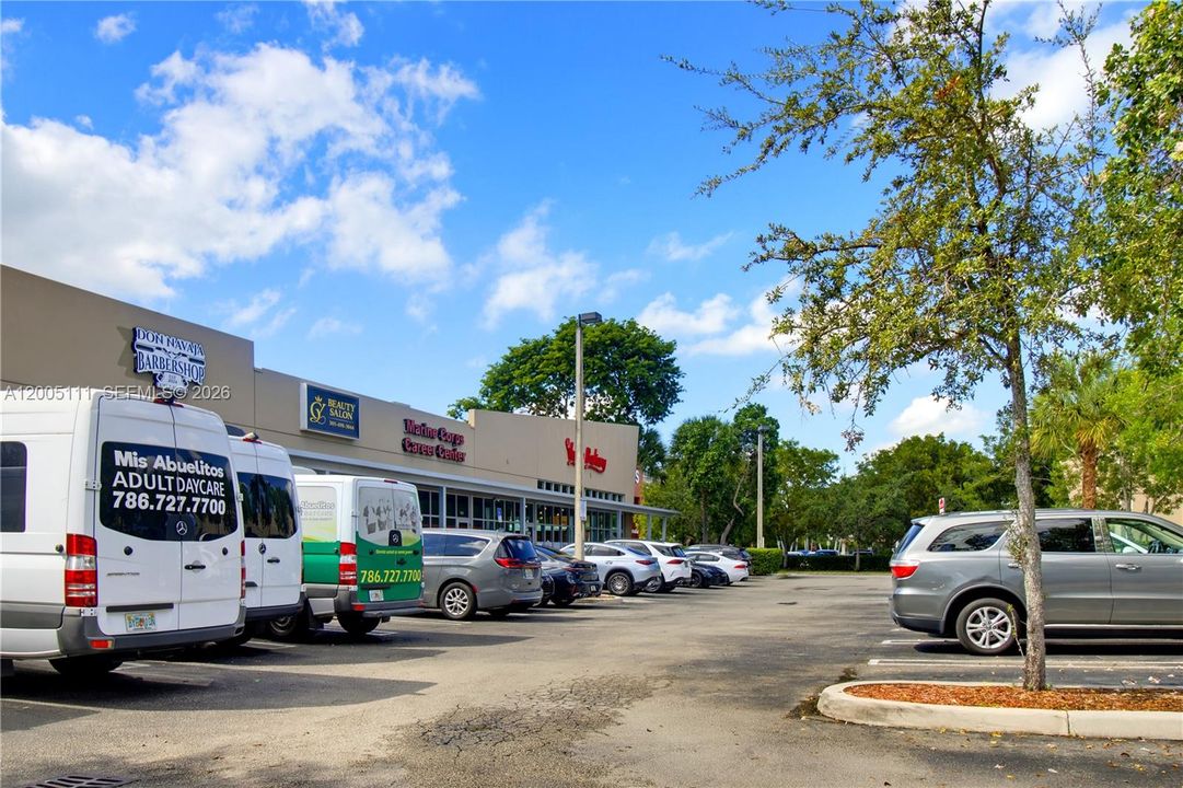 Single-story commercial strip center featuring storefront signage, asphalt surface parking, and mature perimeter landscaping