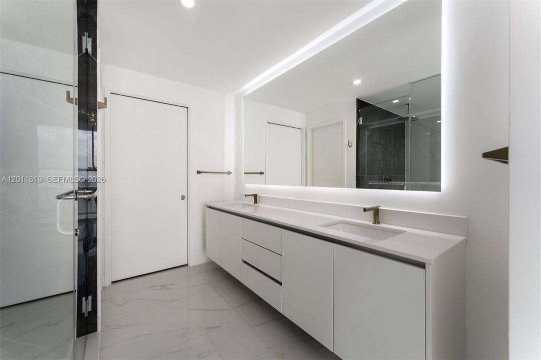 Spa-inspired primary bathroom featuring dual vanities, a deep soaking tub, a frameless glass rainfall shower, and designer porcelain tile throughout.