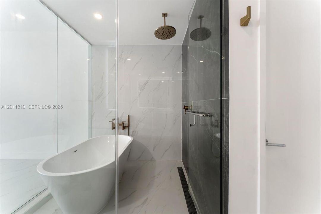 Spa-inspired primary bathroom featuring dual vanities, a deep soaking tub, a frameless glass rainfall shower, and designer porcelain tile throughout.