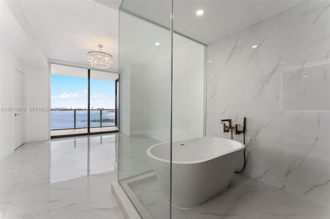 Spa-inspired primary bathroom featuring dual vanities, a deep soaking tub, a frameless glass rainfall shower, and designer porcelain tile throughout.