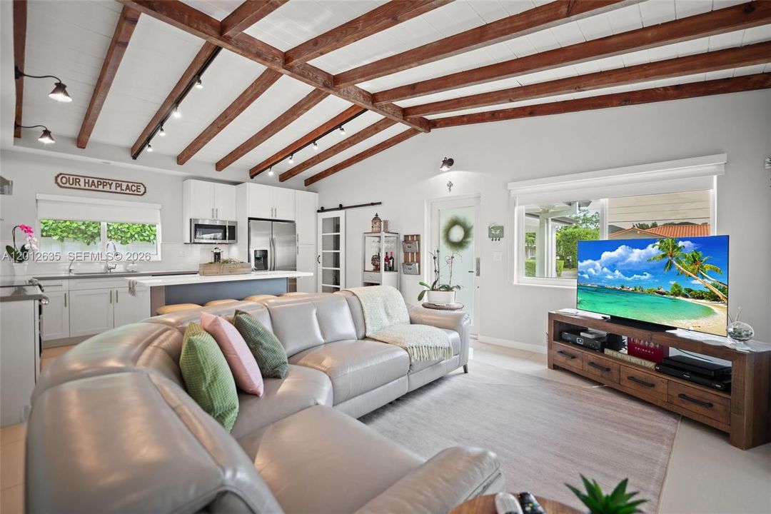 Open-concept living room with vaulted ceilings, exposed wood beams, track lighting,— flows directly into the updated kitchen. Single-family home, Miami FL 33155.