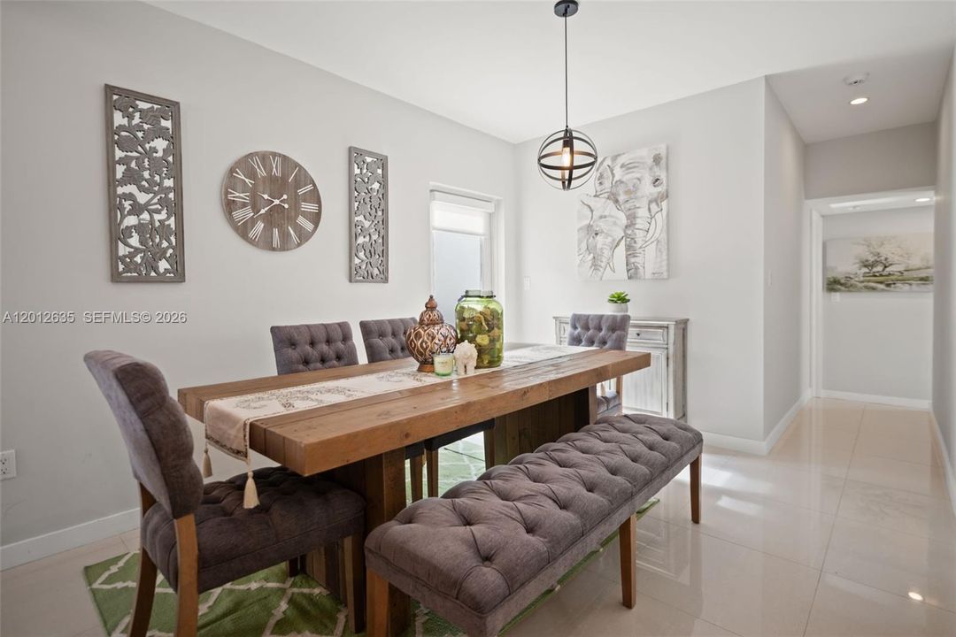 Dedicated dining area with large-format porcelain tile floors, globe pendant light, and open sightlines to hallway — move-in ready, Schenley Park Miami. 33155