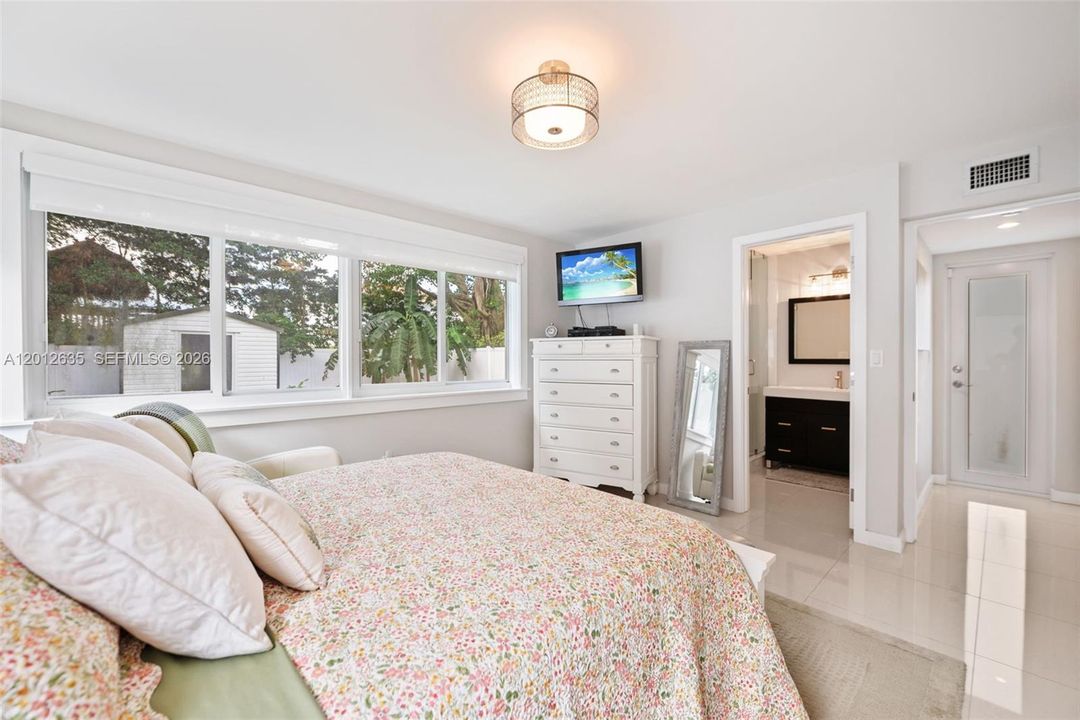 Primary bedroom with large-format porcelain tile floors, impact windows with garden views, dual blackout/sheer shade system, and two walk-in closets with sliding barn doors — Schenley Park, Miami FL 33155.