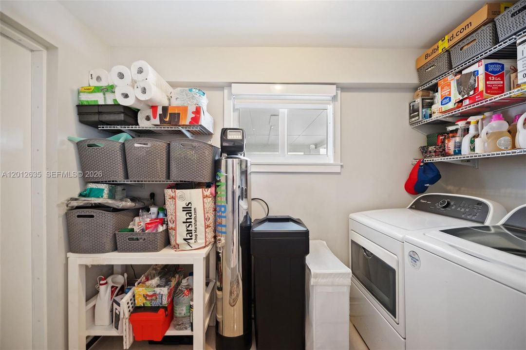 Interior laundry room with full-size Whirlpool washer and dryer, built-in wire shelving, window, and whole-house water purification and softening system — accessed via barn door from kitchen.