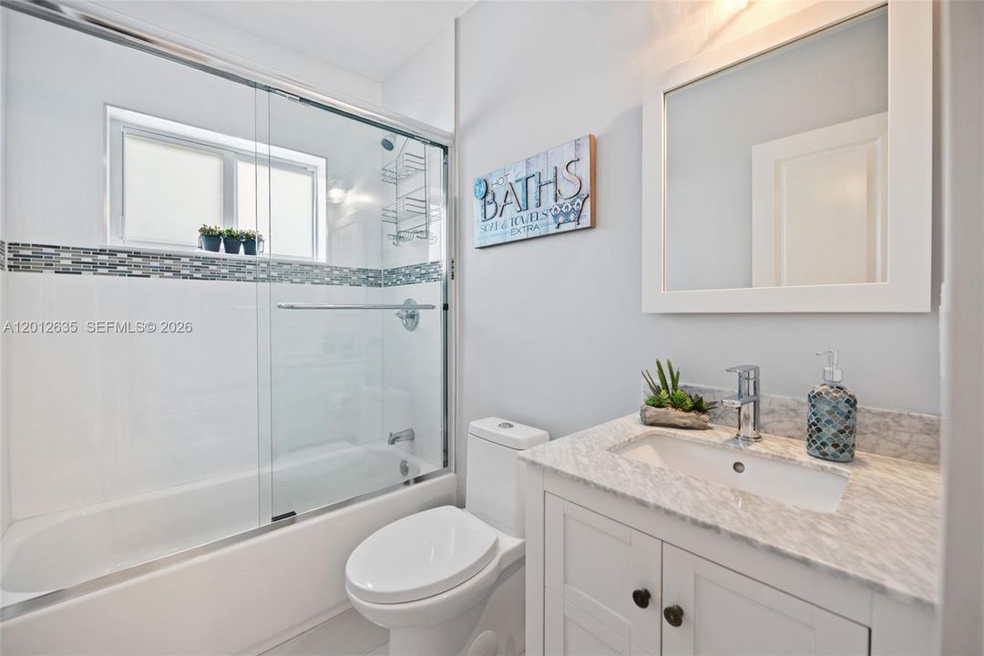 Updated full guest bath with tub/shower combo, sliding glass enclosure, white subway tile with mosaic accent border, white shaker vanity, marble countertop, and chrome fixtures.