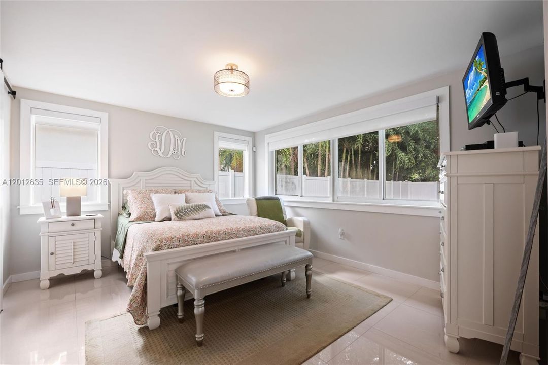 Spacious primary bedroom with large-format porcelain tile floors, dual impact windows with garden views, two walk-in closets with sliding barn doors, and en-suite bath access.