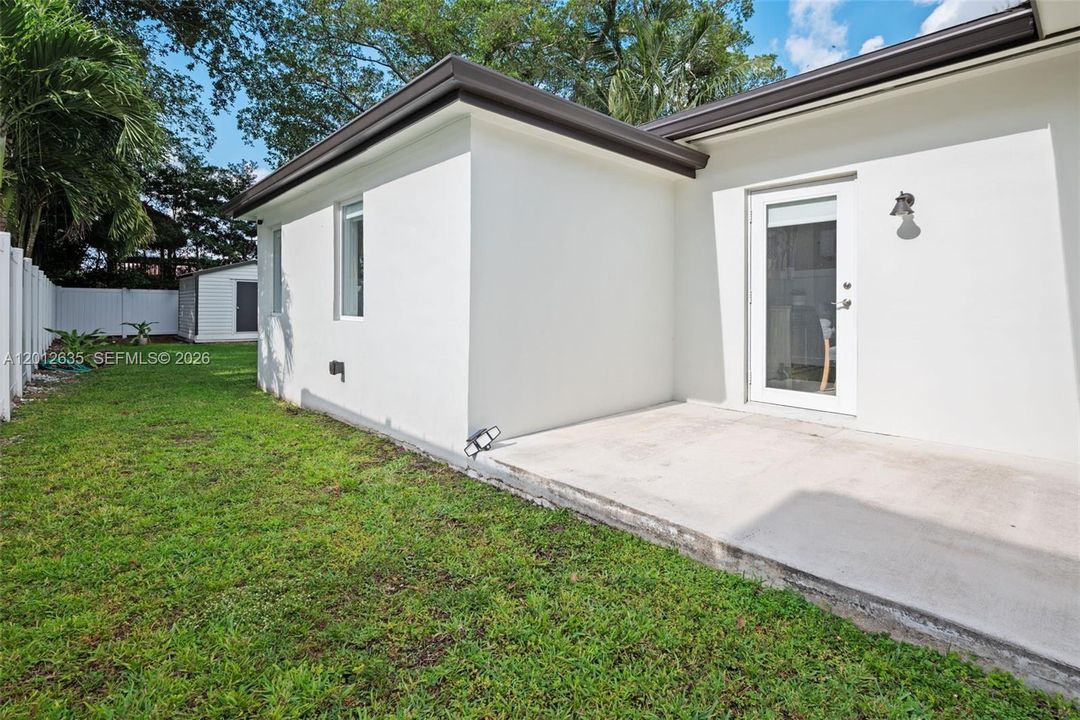 Expansive fenced backyard on 7,500 sq ft lot (50x150) with green lawn, PVC privacy fence, tropical landscaping, and concrete patio — pool-ready