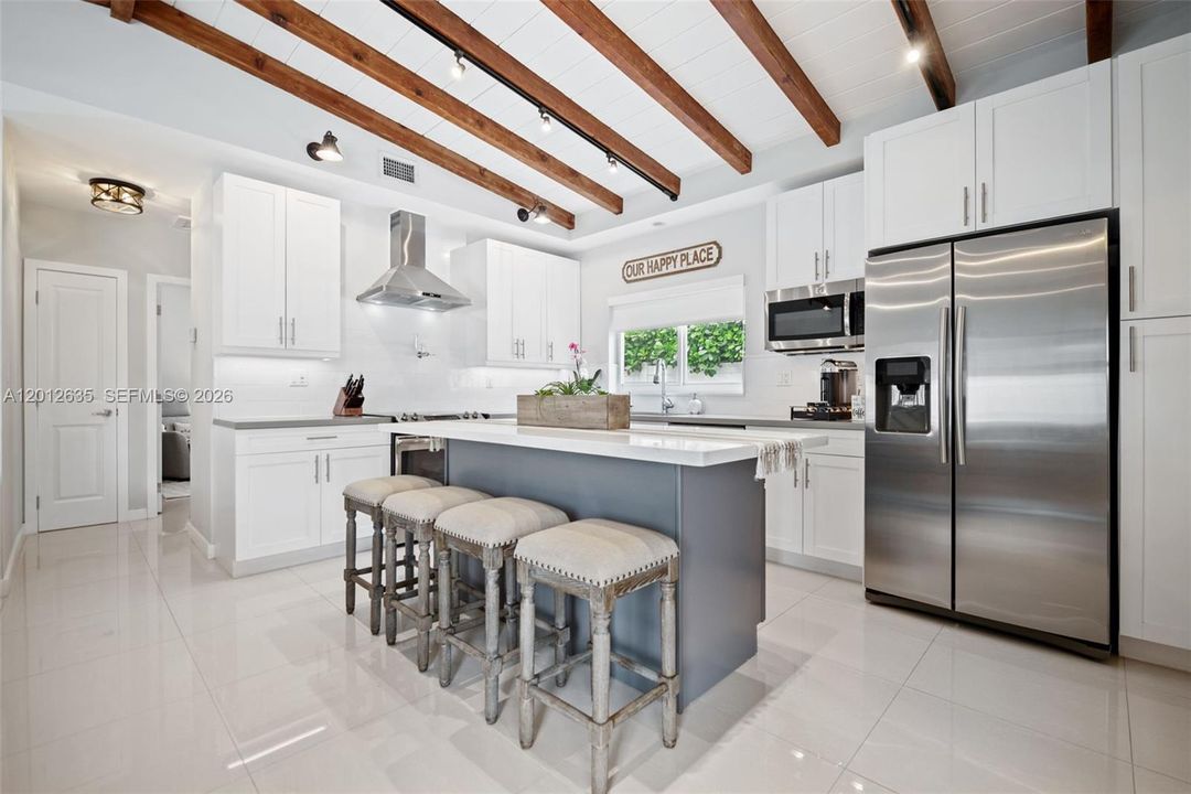 Chef's kitchen with white shaker cabinets, countertops, stainless range hood, GE stainless appliances, subway tile backsplash, and oversized center island with seating for four