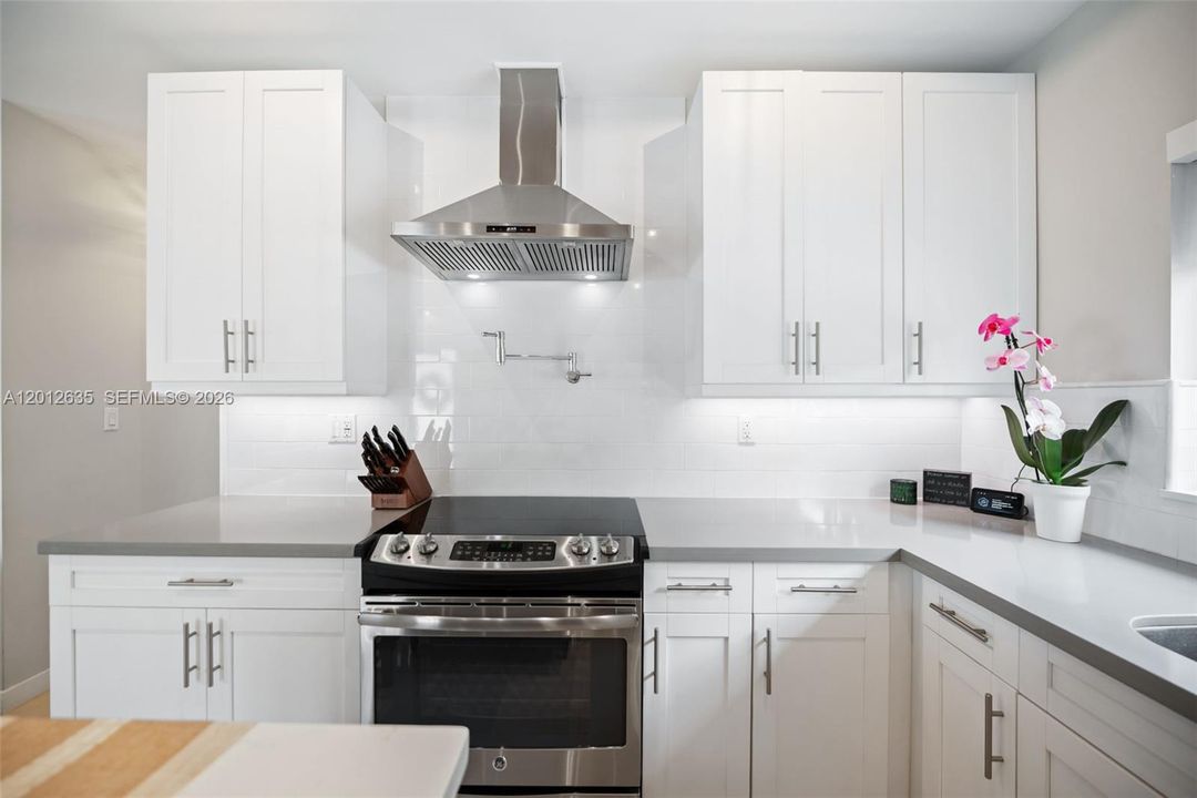 Stainless steel range hood, GE electric range with double oven, pot filler, white subway tile backsplash, and under-cabinet lighting —remodeled kitchen, Miami FL 33155.