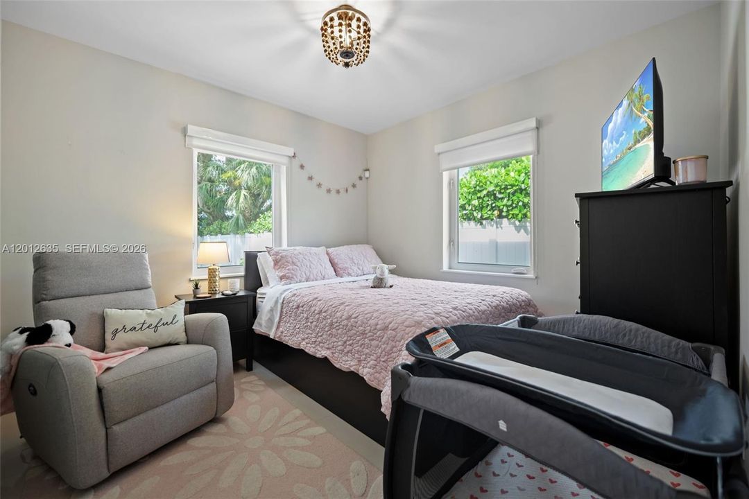 Second bedroom with two impact windows, natural light, neutral tile floors, and decorative ceiling fixture