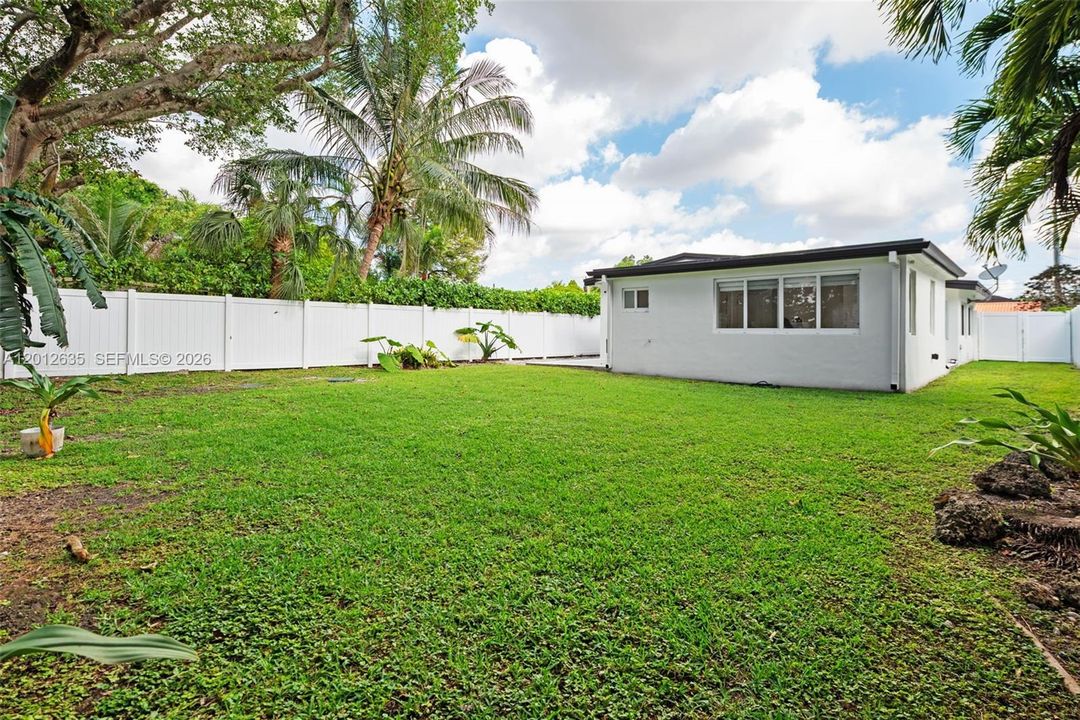 Covered rear concrete patio with French glass door, security lighting, gutters, and fenced backyard with lush lawn, Schenley Park Miami FL 33155.