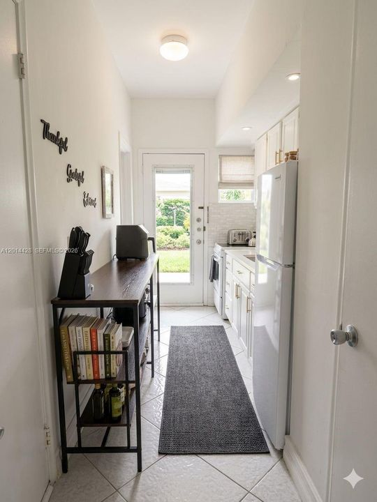 Hallway from living area towards front door and kitchen (with AI generated lighting)