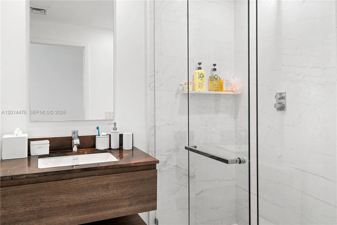 Bathroom – A contemporary bathroom includes a floating wood vanity, dark stone countertop, undermount sink, and a glass-enclosed marble-look shower. Clean white walls and polished finishes give the space a crisp, spa-inspired feel.