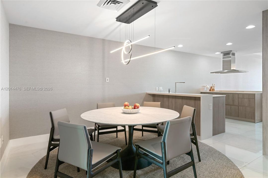 Dining Area – The dining area features a round table, neutral seating, and a sculptural linear chandelier that adds a modern focal point. Its placement beside the kitchen creates an easy flow for everyday dining or hosting.