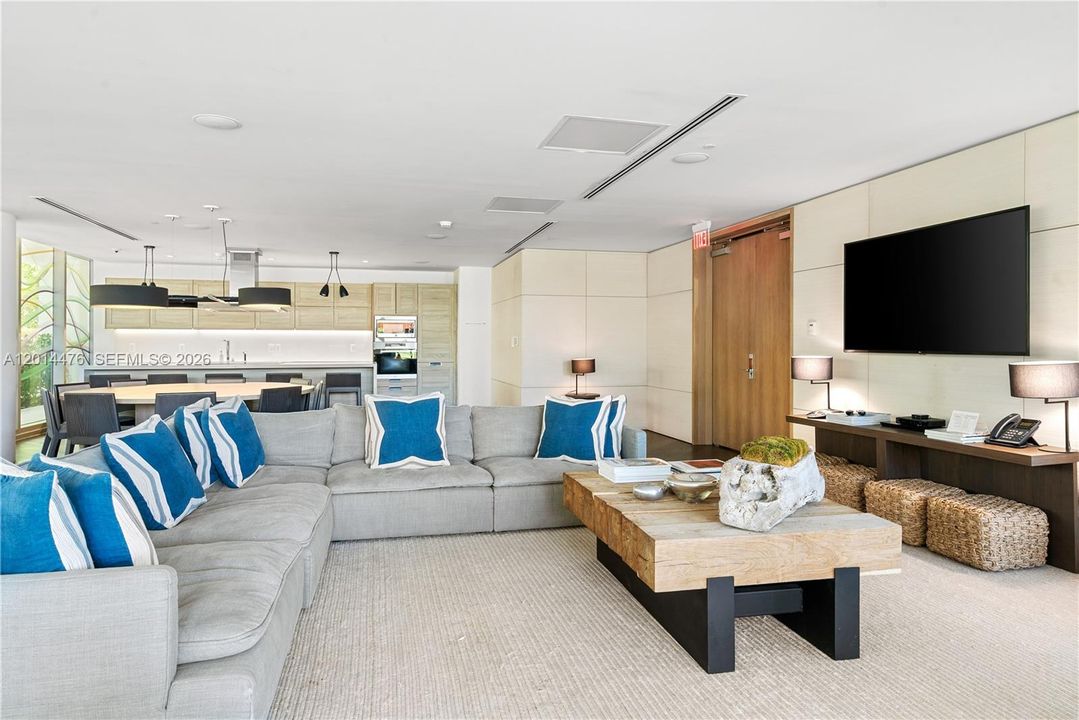 Resident Lounge – A spacious lounge area features comfortable sectional seating, a media wall, and an open connection to the dining and kitchen areas. Natural textures and coastal blue accents create a relaxed, refined gathering space.