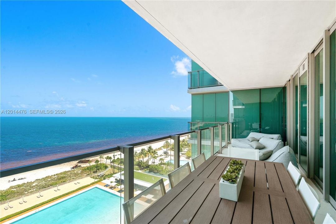 Oceanfront Balcony – The expansive balcony offers outdoor dining and lounge space with glass railings framing wide ocean, beach, and pool views. This open-air setting extends the living space with an impressive coastal backdrop.