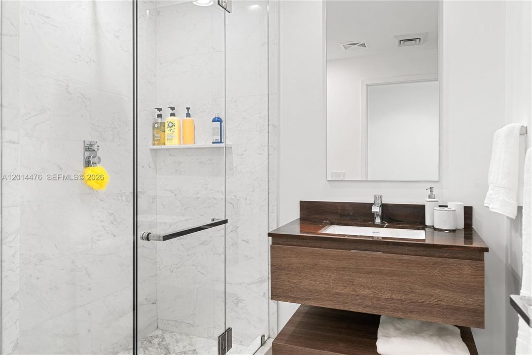 Guest Bathroom – The guest bathroom offers a glass-enclosed shower with marble-look tile, a floating wood vanity, and a dark stone countertop. Bright lighting and minimalist details create a fresh, contemporary design.