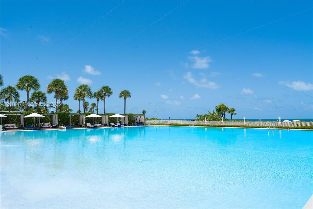 Resort-Style Pool – The pool area features a large beachfront pool surrounded by cabanas, lounge seating, and palm trees. Ocean views beyond the pool create a serene resort-style setting.